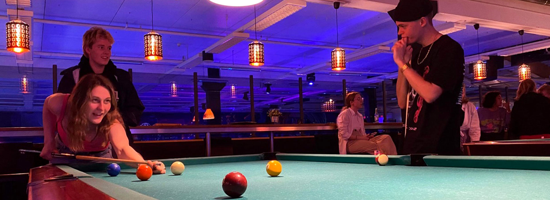 Tre gjester rundt biljardbordet hos Åsane Bowling — varm lampe og blå LED i bakgrunnen